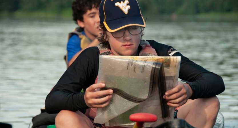 A person wearing a lifejacket sits in a canoe and examines a map